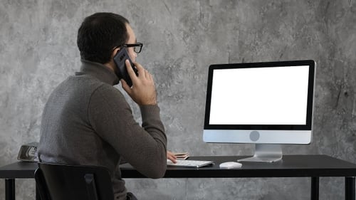 Man talking on phone in office and looking on computer
