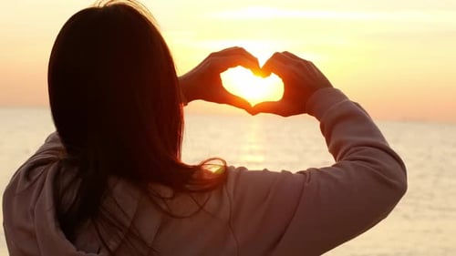 Una mujer hermosa hace un corazón con sus manos al amanecer. La niña se regocija al amanecer
.