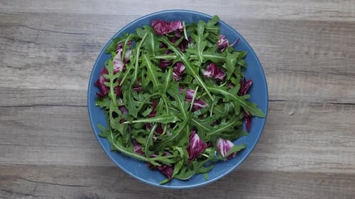 Las hojas de ensalada mezclan bocadillos verdes y jugosos, en un plato, girando sobre una mesa.