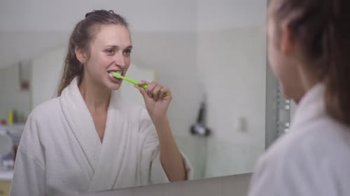 Young Woman Brushing Teeth in Bathroom Mirror