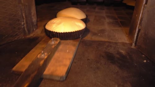 Bäcker legt Brotteig mit Schaufel in den Ofen.