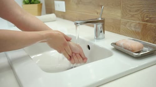 Woman washing hands with soap in bathroom sink