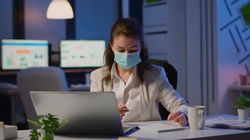 Employé avec masque de protection travaillant tard dans la nuit dans un nouveau bureau normal