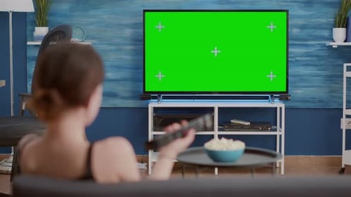 Static Tripod Shot of Young Woman Switching Channels While Looking at Green Screen on Tv