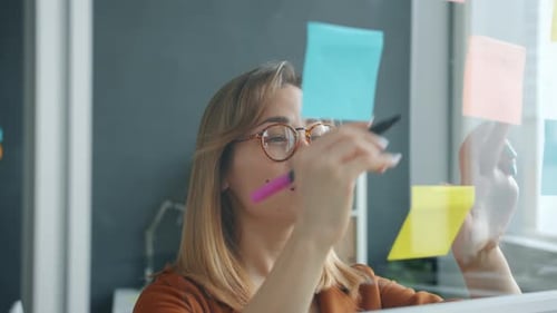 Slow Motion of Creative Businesswoman Writing Info on Sticky Notes on Glass Board in Office