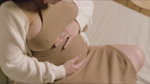 Schwangere Frau sitzt auf dem Bett und berührt den Bauch