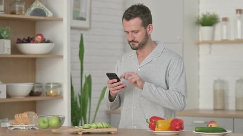 Man in Pajamas Using Smartphone in Kitchen