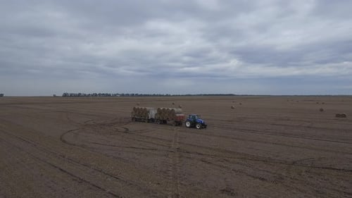 Tractor Pulling Hay Bales in Rural Farm Field