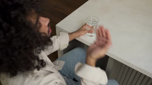Person Holds Pill and Water at Table