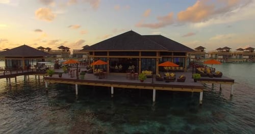 Aerial drone view sunset scenic tropical island, resort hotel with overwater bungalows, Maldives.