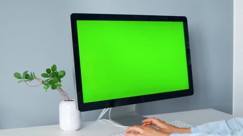 Woman Typing on a Computer Keyboard, Monitor with a Green Screen. Chroma Key. Copy Space.