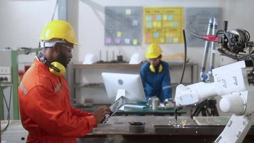 Asiatischer Ingenieur und Techniker steuern die Automatisierung des Roboterarm-Schweißens mit Computerbildschirm