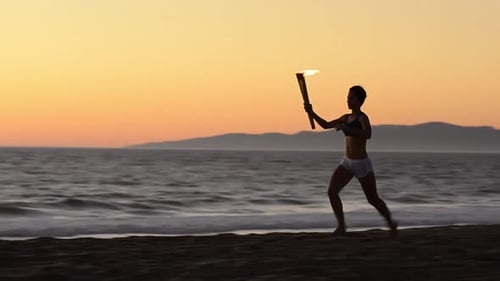 Woman running with a simulated Olympics torch on the beach at sunset.