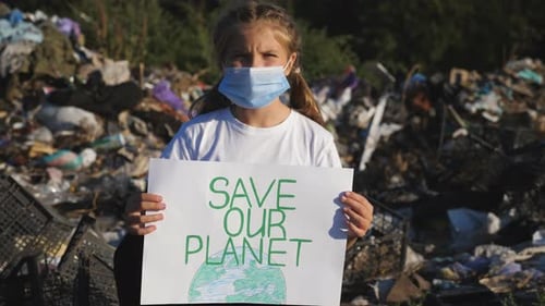 Child Holds Sign in Front of Trash Pile