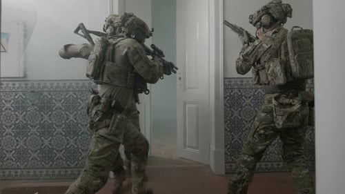 Bewaffnete Männer öffnen Tür eines zerstörten Gebäudes mit Fuß