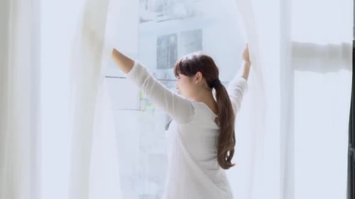 Woman Stretching Arms Opening Curtains in Bright Room