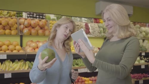 Women Use Tablet While Shopping for Fruit