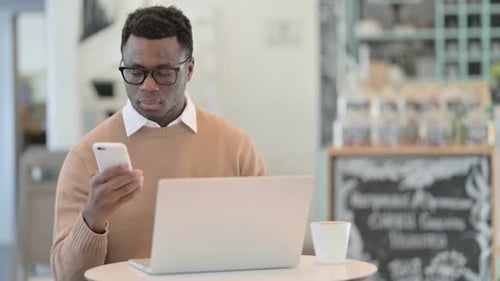 Young Man Uses Phone and Laptop Indoors