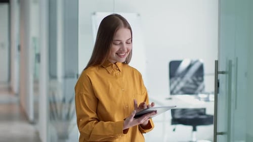 Young Happy Lady Employee Web Surfing on Digital Tablet and Smiling Standing at Office Corridor Free