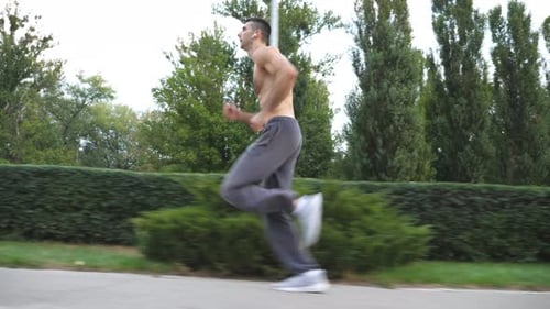 Young Muscular Sportsman Sprinting Fast Along Trail Near Forest at Summer Day