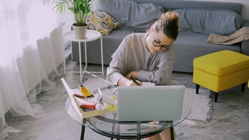 Woman Writing in Notebook While Using Laptop