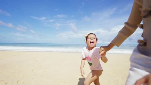 4K Asian mother holding hands with little daughter walking together at the beach in sunny day.