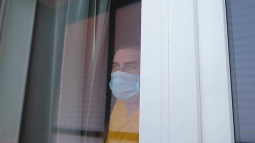 Coronavírus pandêmico COVID-19. Homem de quarentena com máscara médica no rosto olhando pela janela
