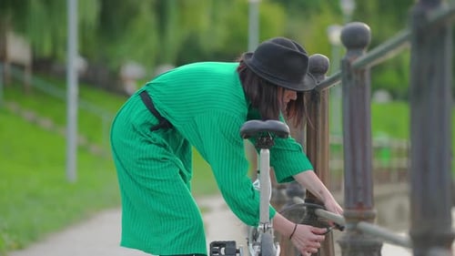 Woman Locks Bicycle in Urban Park