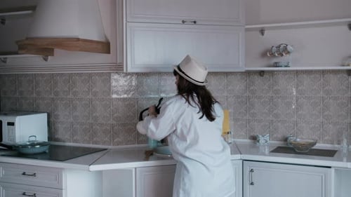Woman Dances in the Kitchen With Teapot and Spoon