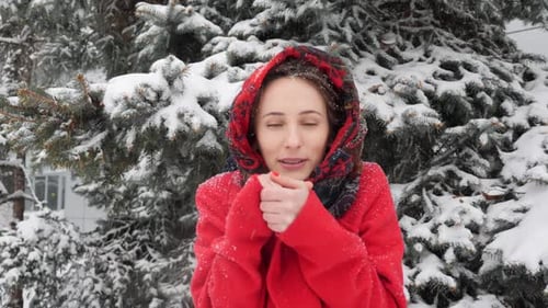 Beautiful Young Woman Trying to Warm Frozen Hands with Breath and Warm up In Red Winter Coat