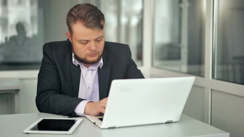 Junger Geschäftsmann, der im Büro sitzt am Schreibtisch und schaut auf Laptop-Computerbildschirm