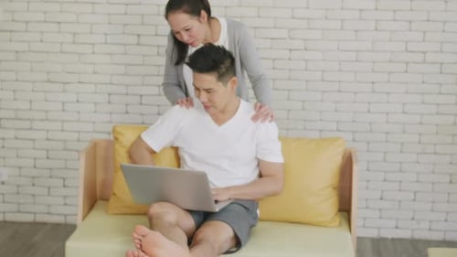 family couple husband and wife laughing sitting on sofa using laptop computer working from home
