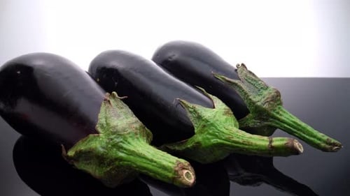 Fresh Shiny Eggplants on a Black Reflective Surface