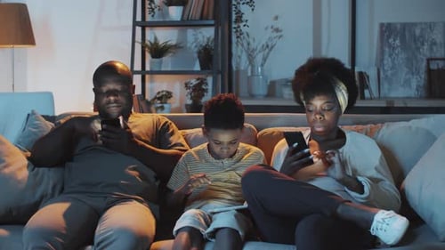 Family Uses Electronic Devices on Couch at Night