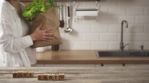 Sobre la
mesa de la cocina, recubierta de cubos con la palabra «Salva la Tierra». Mujer lleva una bolsa de papel y la coloca cerca