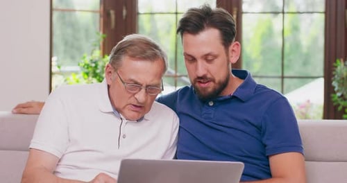Senior Man and Young Adult with Laptop Indoors