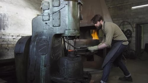 Bearded Blacksmith Forging Hot Metal with Machine