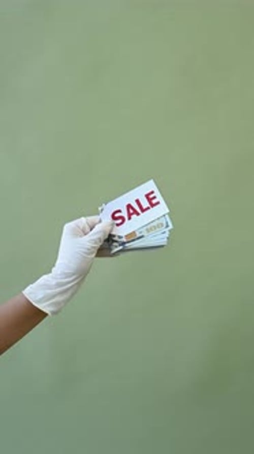 Hand in Glove Holding Sale Sign over Money