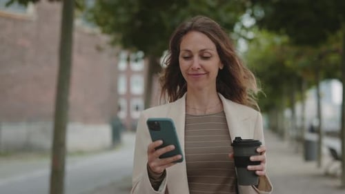 Woman with Phone and Coffee Walking in City