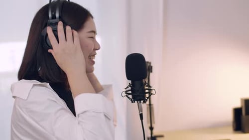 Woman Singing into Microphone with Headphones in Studio