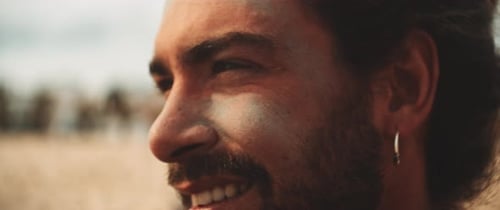 Closeup of a young man smiling and wearing green sunscreen at the beach