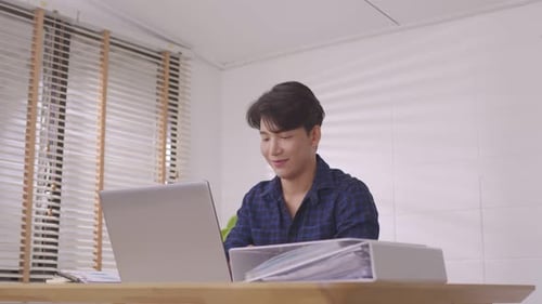 At home, a business asian man types and works online on a desk table with a laptop.