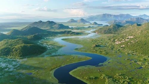 Bends and curves of blue river flowing through green valley toward distant mountains.