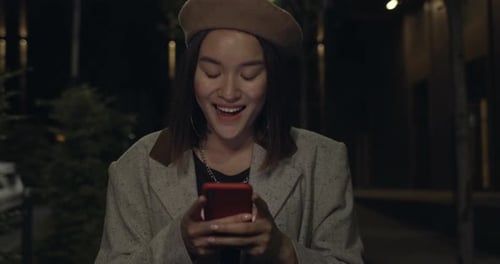 Crop View of Attractive Female Person Using Smartphone While Walking at Night Street. Young Cheerful