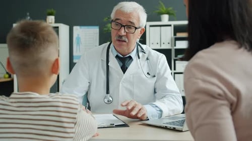 Experienced Paediatrist Talking To Mother and Child Writing in Medical Record in Clinic