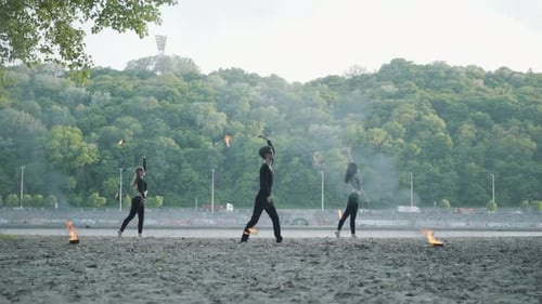 Junger schlanker Mann und zwei schöne Frauen führen gleichzeitig Show mit Flame auf