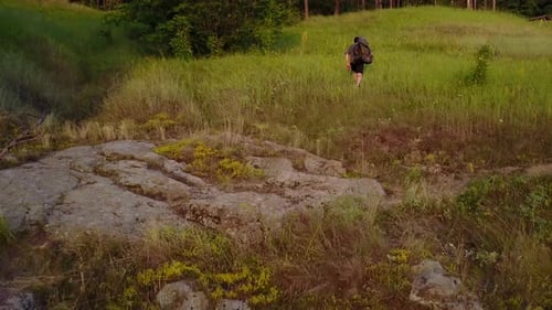 Backpacker Hiking Up Grassy Hill at Sunrise