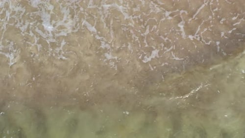 VISTA AÉREA: Vista desde arriba de cerca de las olas chocando en la costa poco profunda