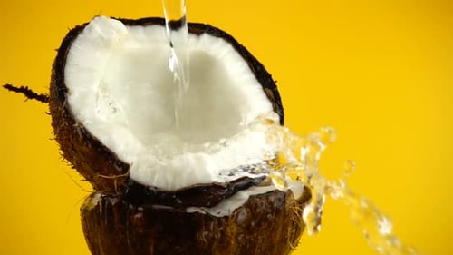 Pouring Water onto Halved Coconut on Yellow Background