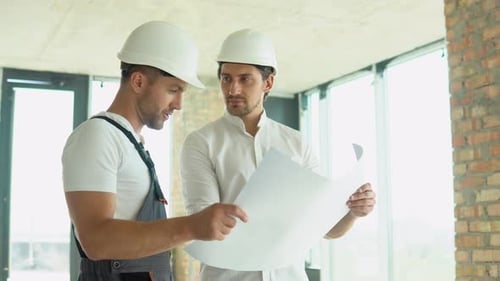 Dois jovens engenheiros em um capacete de segurança em pé no canteiro de obras segurando uma planta do